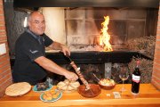 Julio, junto a las brasas, muestra sobre la mesa un pincho de lechazo alrededor de varios platos