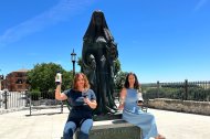 Helena Muelas y su hermana Reyes sentadas a los pies de la escultura de la Reina Juana, frente a las casas del Tratado en Tordesillas.
