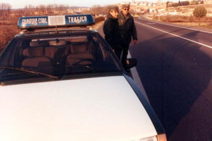 Agentes junto a vehículo oficial estacionado en arcén de travesía. 1995