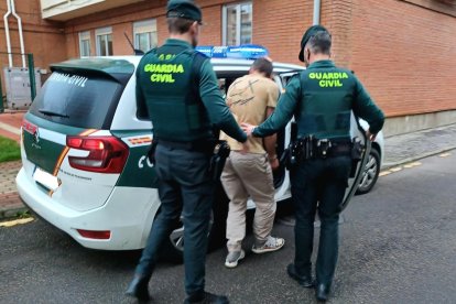 Dos agentes de la Guardia Civil meten al detenido en el coche.