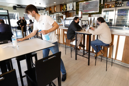 Un camarero desinfecta la mesa de un bar el día antes del cierre del interior de la hostelería mientras unos clientes disfrutan de su consumición. / J.M. LOSTAU