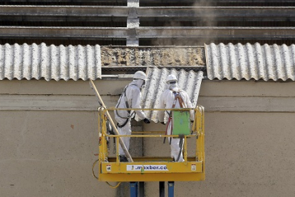 Dos trabajadores retiran placas de uralita con amianto en el tejado de una nave industrial de Valladolid. ical