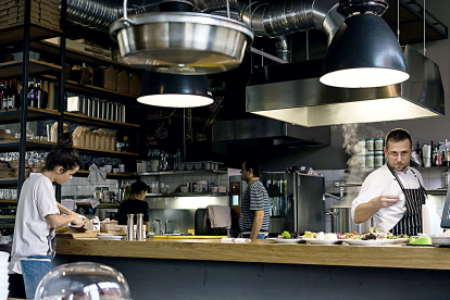 Un chef, dos ayudantes y una camarera atienden la cocina de un restaurante .-PQS/CCO