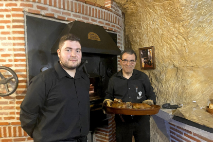 Julio y su hijo Pablo, frente al horno en el que asan el lechazo en La Cueva de Mucientes. Tras ellos, una foto de Julio Romo, fundador de la bodega.