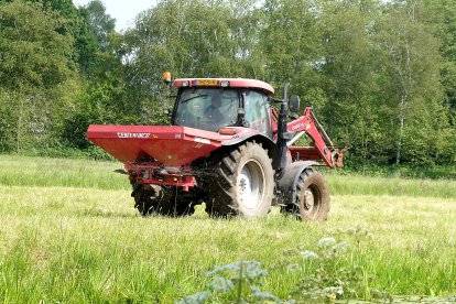 Un agricultor trabaja en un cultivo a bordo de un tractor con esparcidor de fertilizante