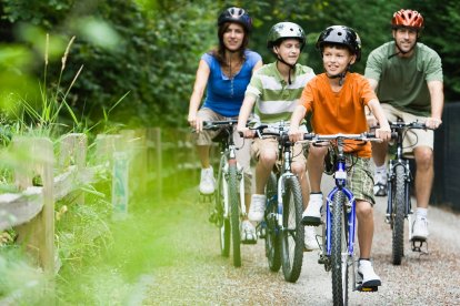 Familia con dos niños montando en bicicleta por un camino natural rodeado de vegetación, en un entorno seguro y tranquilo ideal para rutas familiares