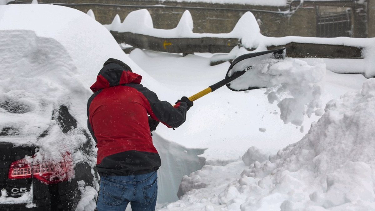 Un hombre retira la gran cantidad de nieve acumulada en su vehículo estacionado en el Puerto de Pajares de León.- ICAL