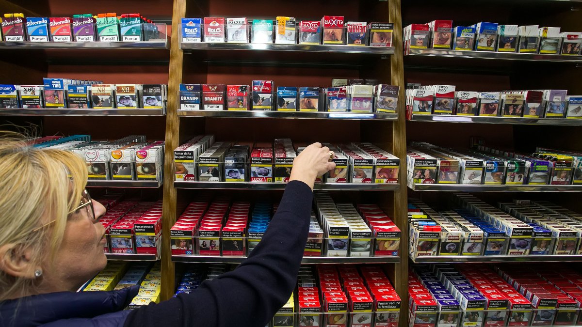 La dependienta de un estanco coge una cajetilla de tabaco del casillero.