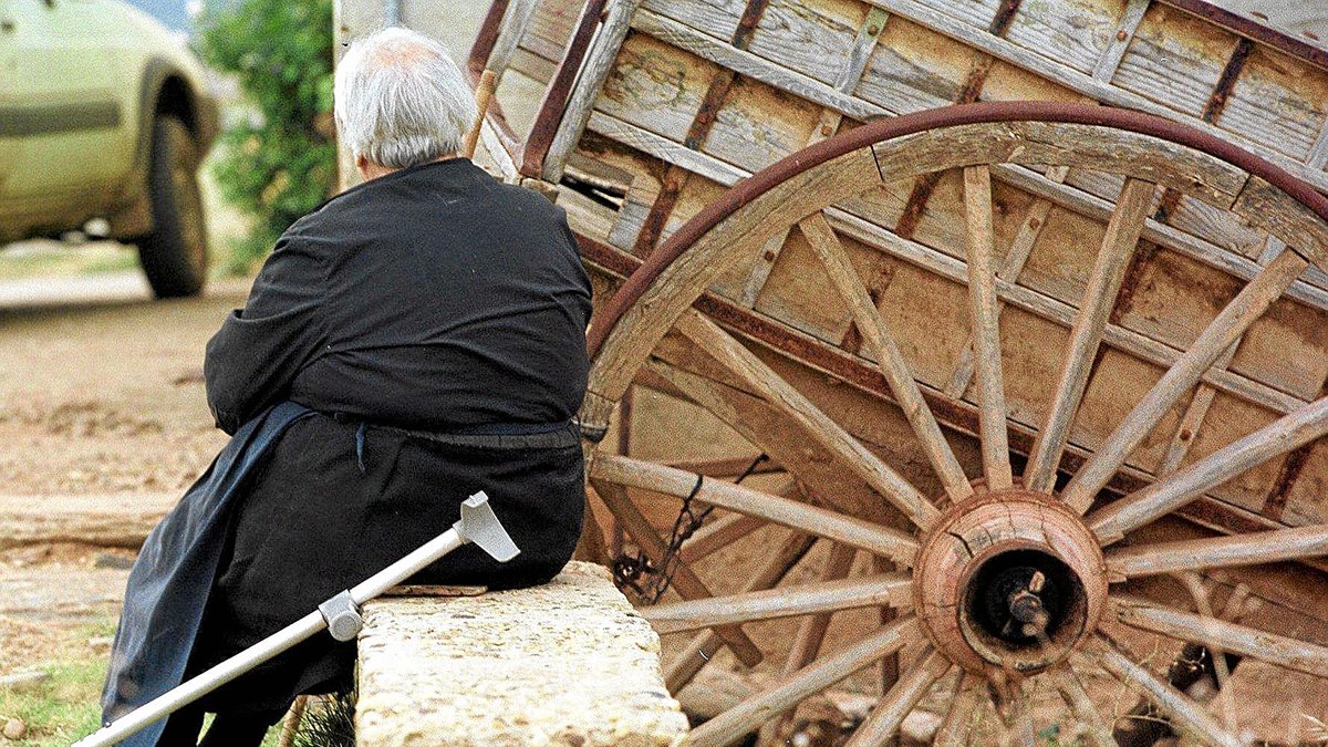 UNA MUJER ANCIANA DESCANSA SENTADA JUNTO A UN CARRO Y SU MULETA