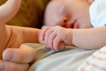 Un bebé agarra el dedo de su madre mientras duerme en su cuna. PQS / CCO