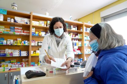 Una farmacéutica atiende a una clienta, ambas con mascarilla.- ICAL