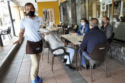 Un camarero atiende la terraza del bar ‘Peña’ en la localidad vallisoletana de Villalón de Campos. Arriba, Ramón Montoya acarrea piedras en Treviño. Abajo, un grupo de vecinos charla en Hinojosa del Campo .  SGC / RAÚL OCHOA / L. TEJEDOR