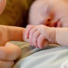 Un bebé agarra el dedo de su madre mientras duerme en su cuna. PQS / CCO