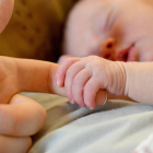 Un bebé agarra el dedo de su madre mientras duerme en su cuna. PQS / CCO