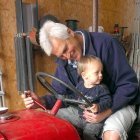 Un agricultor veterano muestra a su nieto los mandos de un viejo tractor en una explotación agraria
