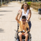 Álex saluda con las pulseras que ha hecho en el campamento y luce su colgante de arcilla, empujado en silla de ruedas por su madre, Leticia Merino.- PHOTOGENIC