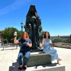 Helena Muelas y su hermana Reyes sentadas a los pies de la escultura de la Reina Juana, frente a las casas del Tratado en Tordesillas.