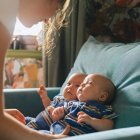 Una madre cuida a sus bebés gemelos en casa, una escena cotidiana que ilustra la realidad de las familias con partos múltiples