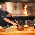 Julio, junto a las brasas, muestra sobre la mesa un pincho de lechazo alrededor de varios platos