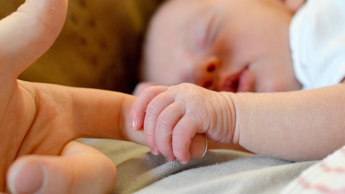 Un bebé agarra el dedo de su madre mientras duerme en su cuna. PQS / CCO