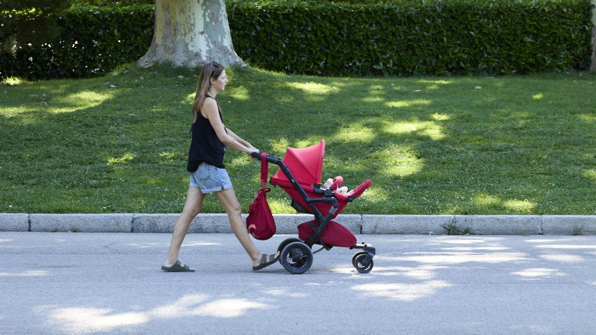 Una mujer pasea con un carrito de bebé en un parque. 