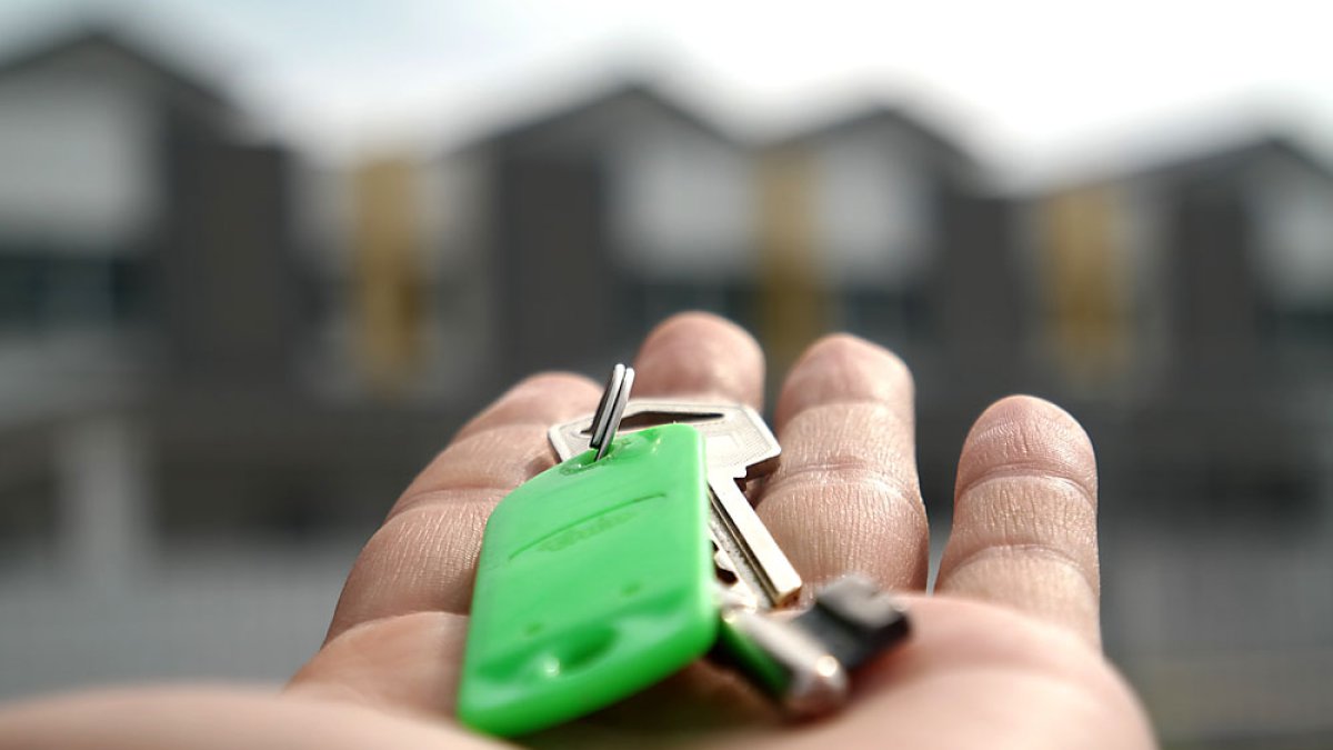Un joven muestra la llave de su vivienda frente a una promoción de adosados. PQS / CCO