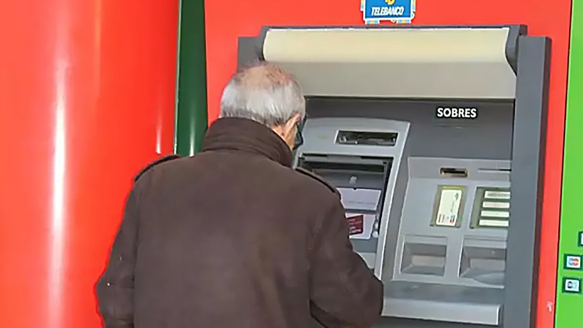 Una persona mayor utiliza un cajero automático en el exterior de una sucursal bancaria.