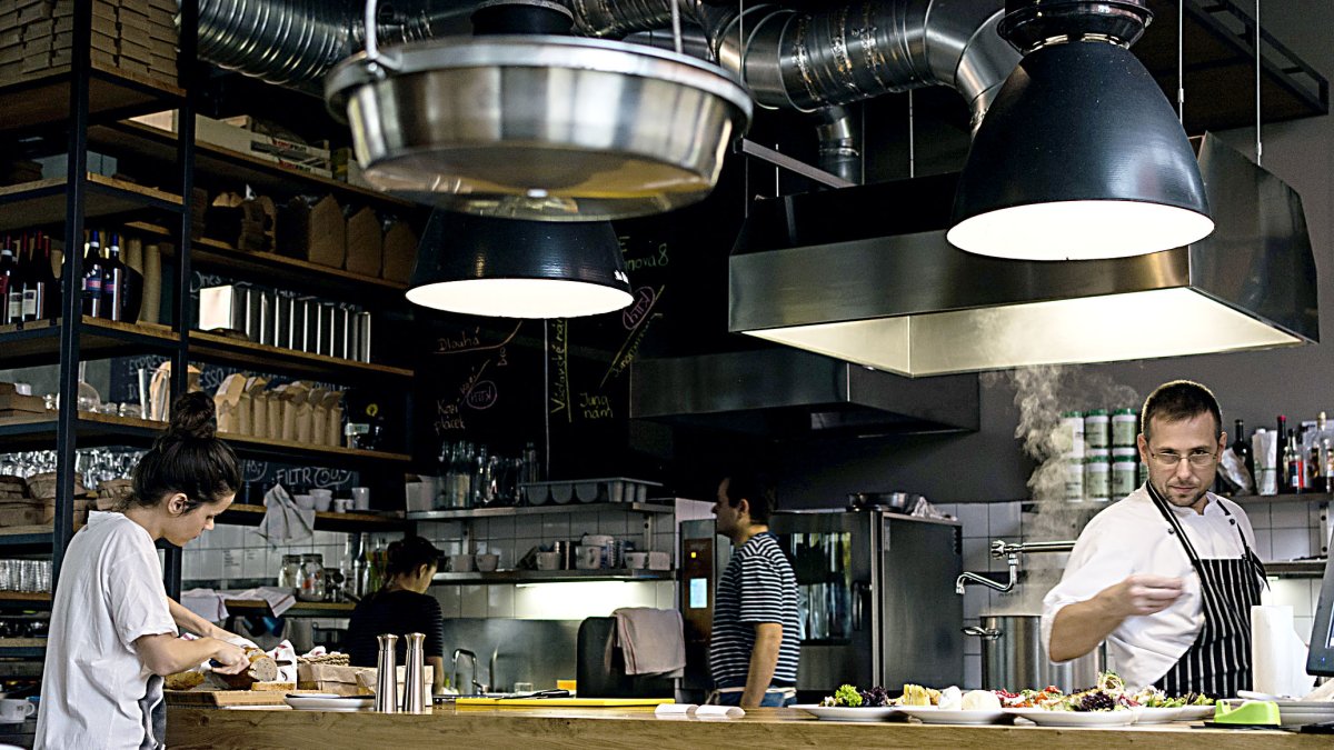 Un chef, dos ayudantes y una camarera atienden la cocina de un restaurante .-PQS/CCO