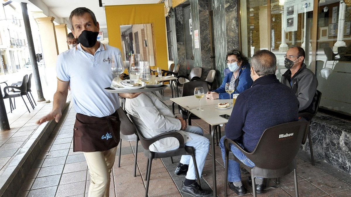 Un camarero atiende la terraza del bar ‘Peña’ en la localidad vallisoletana de Villalón de Campos. Arriba, Ramón Montoya acarrea piedras en Treviño. Abajo, un grupo de vecinos charla en Hinojosa del Campo . SGC / RAÚL OCHOA / L. TEJEDOR