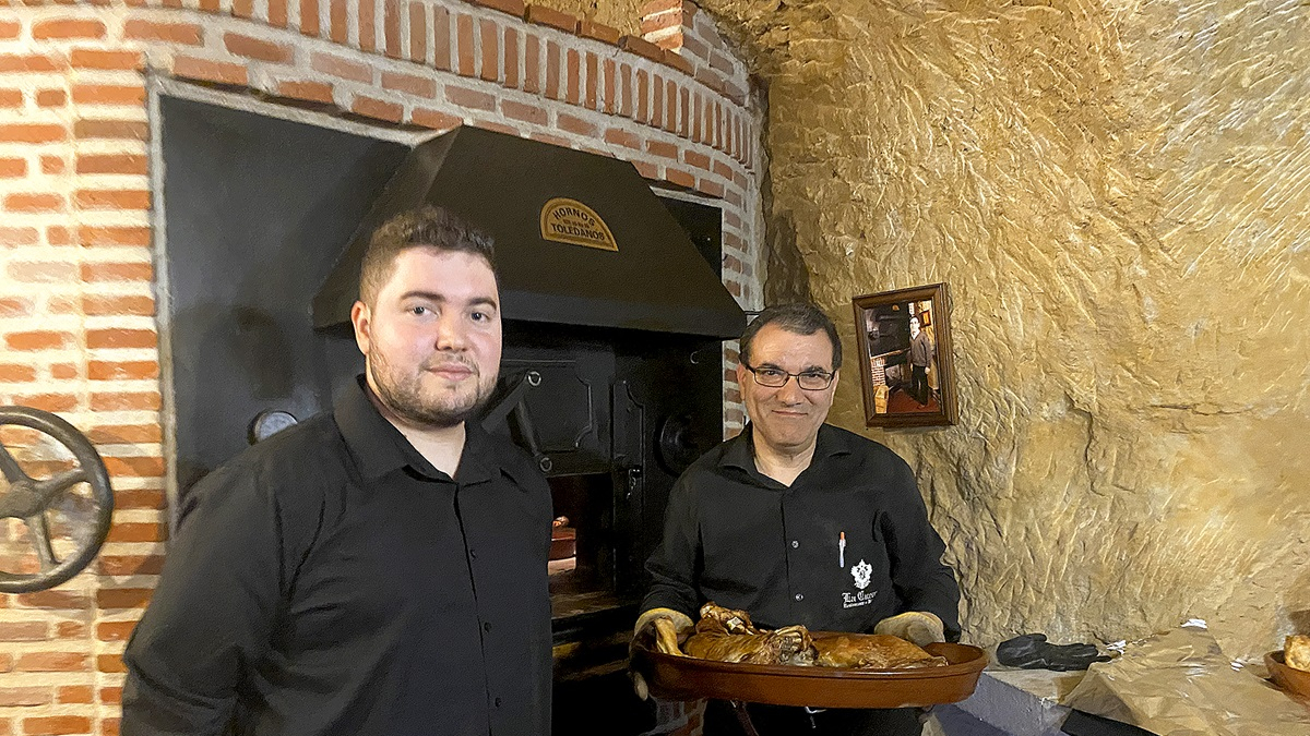 Julio y su hijo Pablo, frente al horno en el que asan el lechazo en La Cueva de Mucientes. Tras ellos, una foto de Julio Romo, fundador de la bodega.