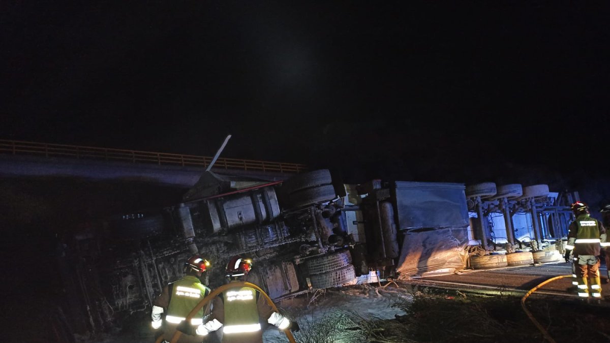 Dos bomberos con el camión volcado en la autovía de León.