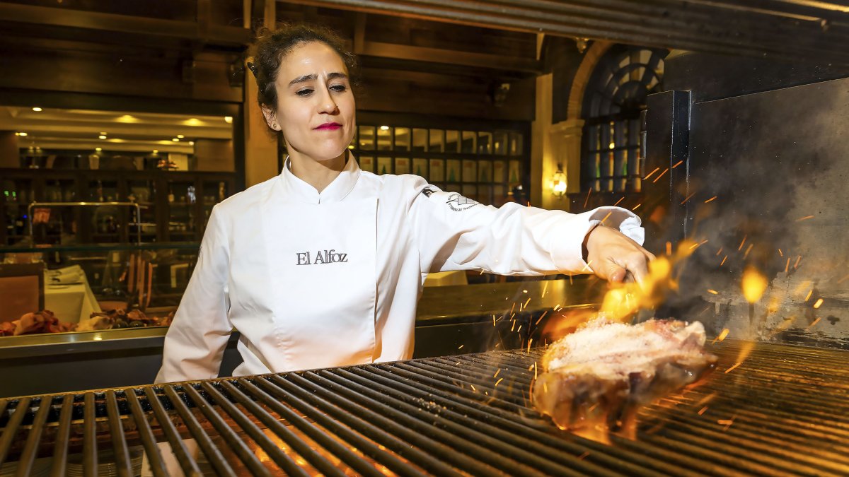 Vanesa Martín maneja las llamas de su flamante parrilla en El Alfoz para cocinar una chuleta. Tras ella, el salón en el que los comensales pueden apreciar su trabajo