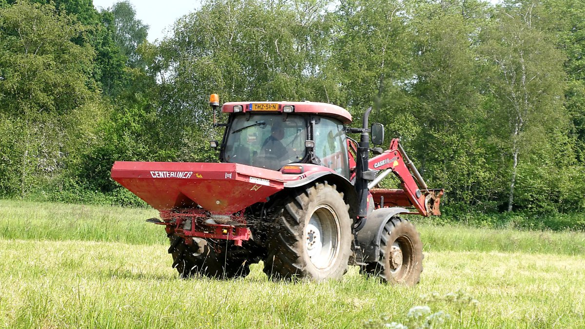 Un agricultor trabaja en un cultivo a bordo de un tractor con esparcidor de fertilizante