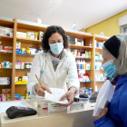 Una farmacéutica atiende a una clienta, ambas con mascarilla.- ICAL