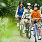 Familia con dos niños montando en bicicleta por un camino natural rodeado de vegetación, en un entorno seguro y tranquilo ideal para rutas familiares